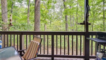 Enjoy al fresco dining on the deck with a forest view, featuring a grill and comfortable seating.