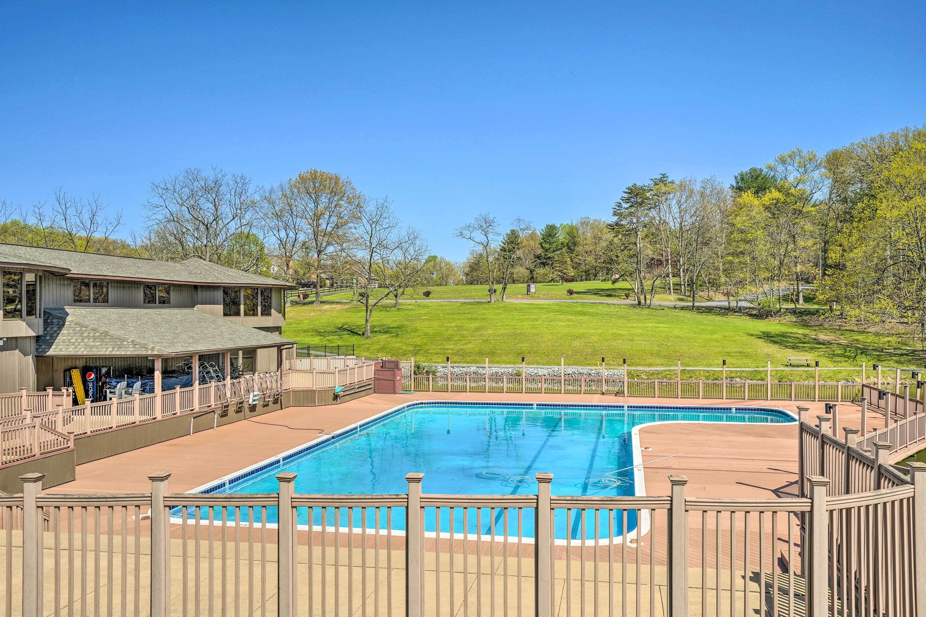 A rectangular swimming pool with a wooden deck and a fence, surrounded by a grassy area and trees.