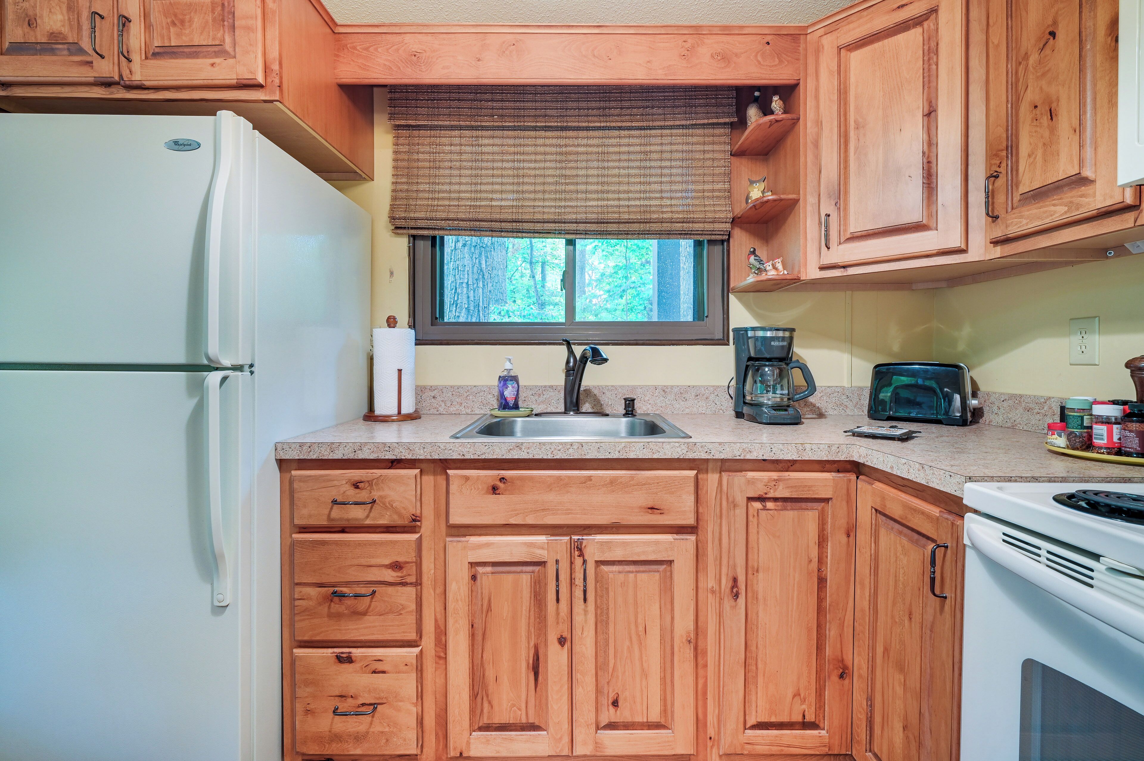 A kitchen with wooden cabinets, a refrigerator, a sink, a window with a blind, and various appliances.