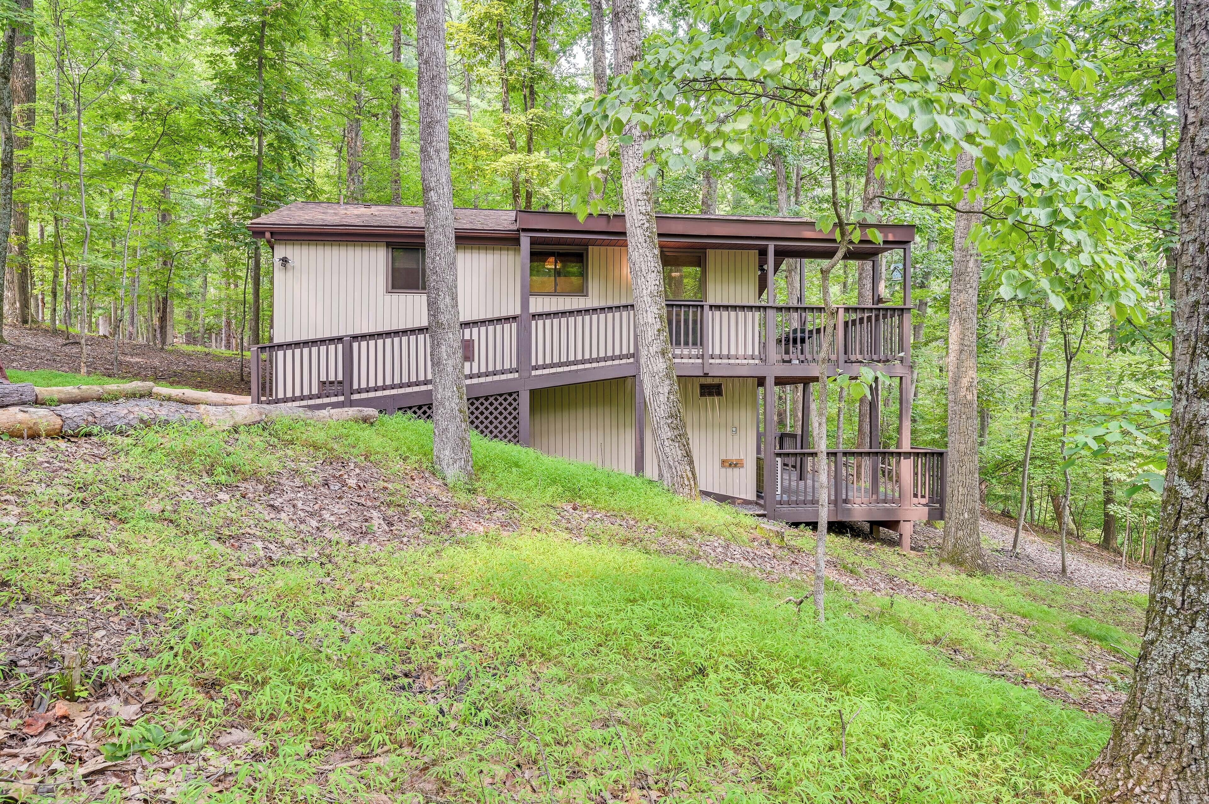 A two-story cabin with a balcony, surrounded by a forested area.