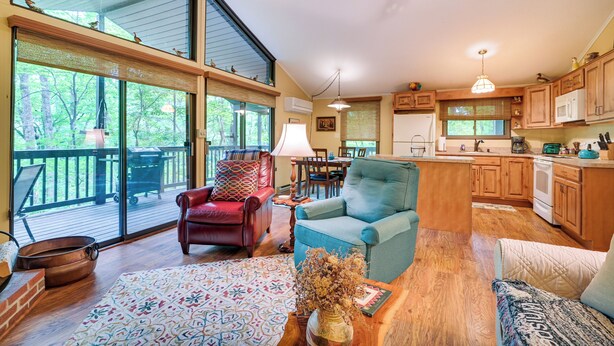 A spacious living area with a large window, a fireplace, a dining table, and a kitchen with wooden cabinets.