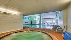 A swimming pool with a hot tub, a changing room, and a seating area with a blue bench.