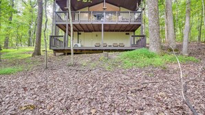 A two-story cabin with a balcony, surrounded by a forest.