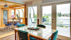 Un coin repas avec une table en bois, des chaises bleues et une vue sur un lac, visible à travers de grandes portes-fenêtres coulissantes.