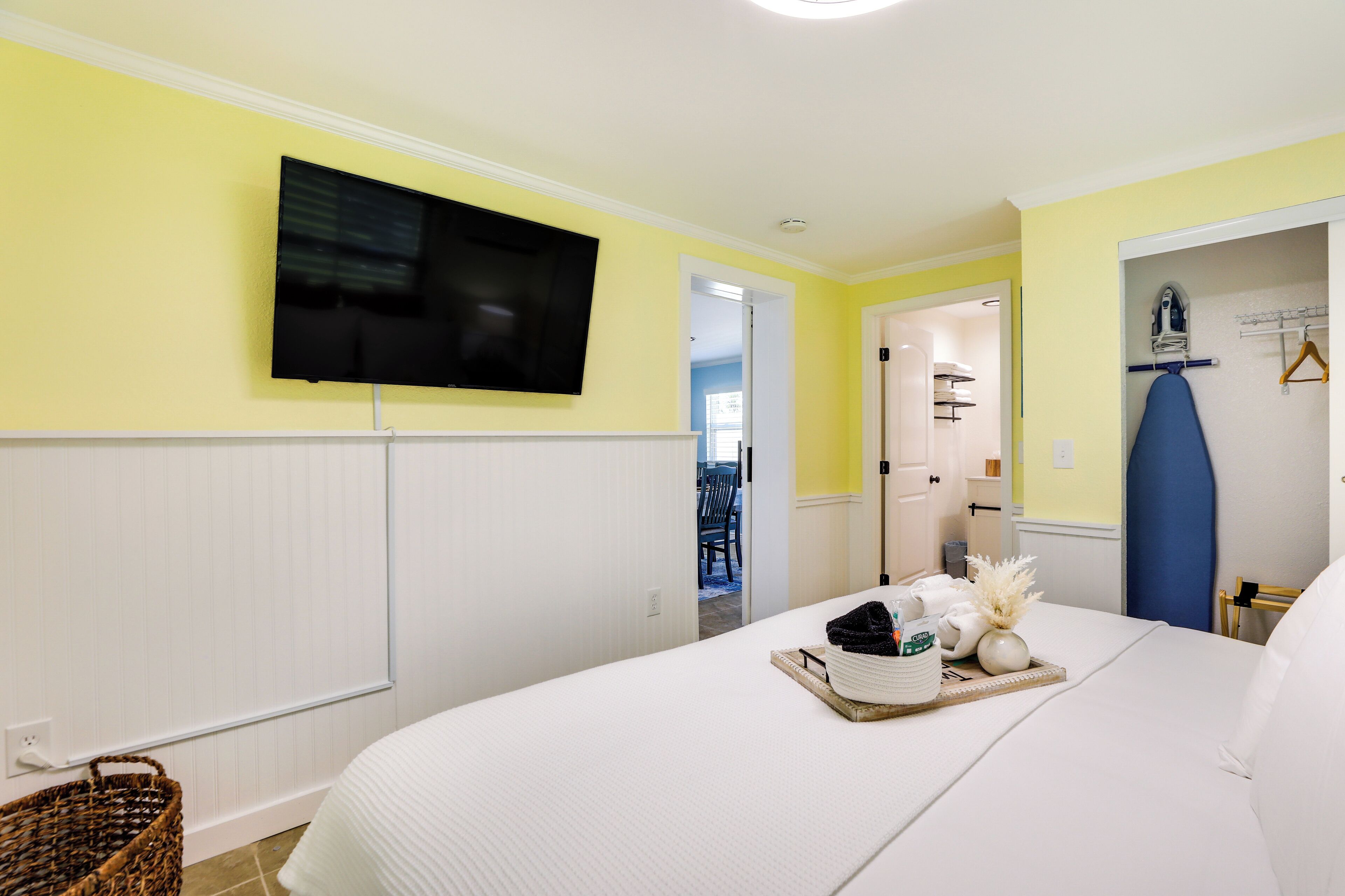 Ein Schlafzimmer mit einem Bett, einem an der Wand befestigten Fernseher und einer Tür zu einem weiteren Raum.
