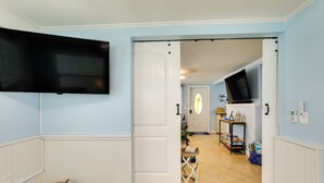 Ein Flur mit einem an der Wand befestigten Fernseher, einer weißen Tür und einem kleinen Tisch mit Pflanze und Büchern.