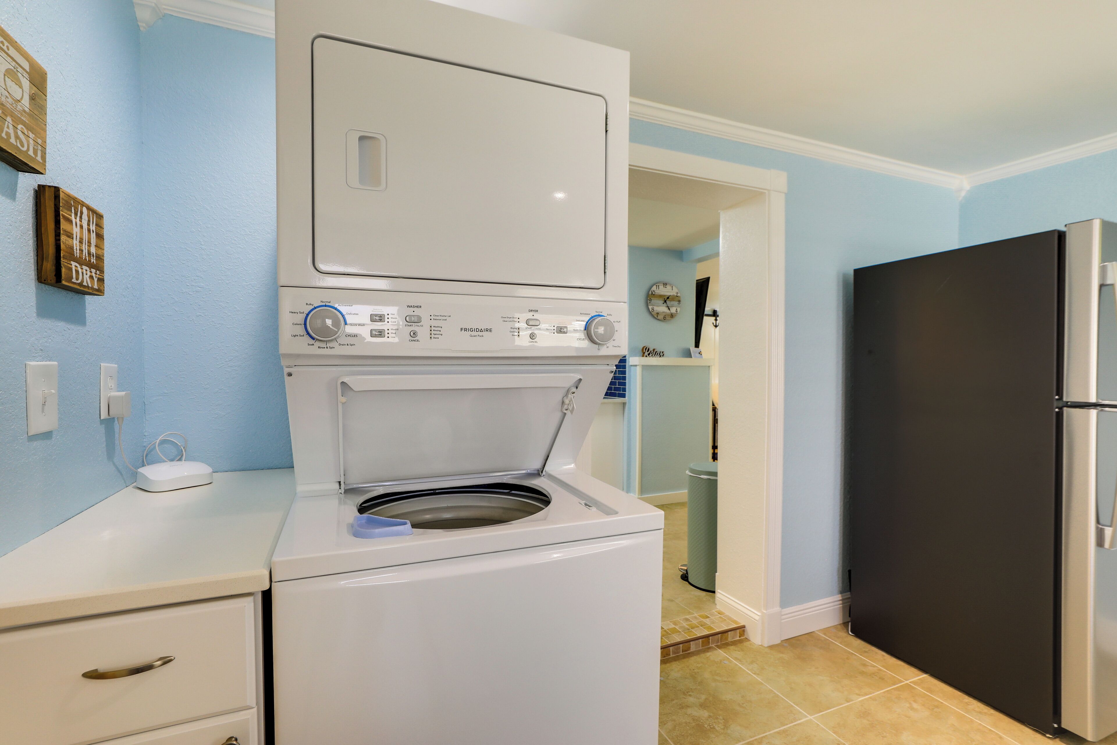 A compact laundry area with a front-loading washer and dryer, a small countertop, and a black refrigerator.