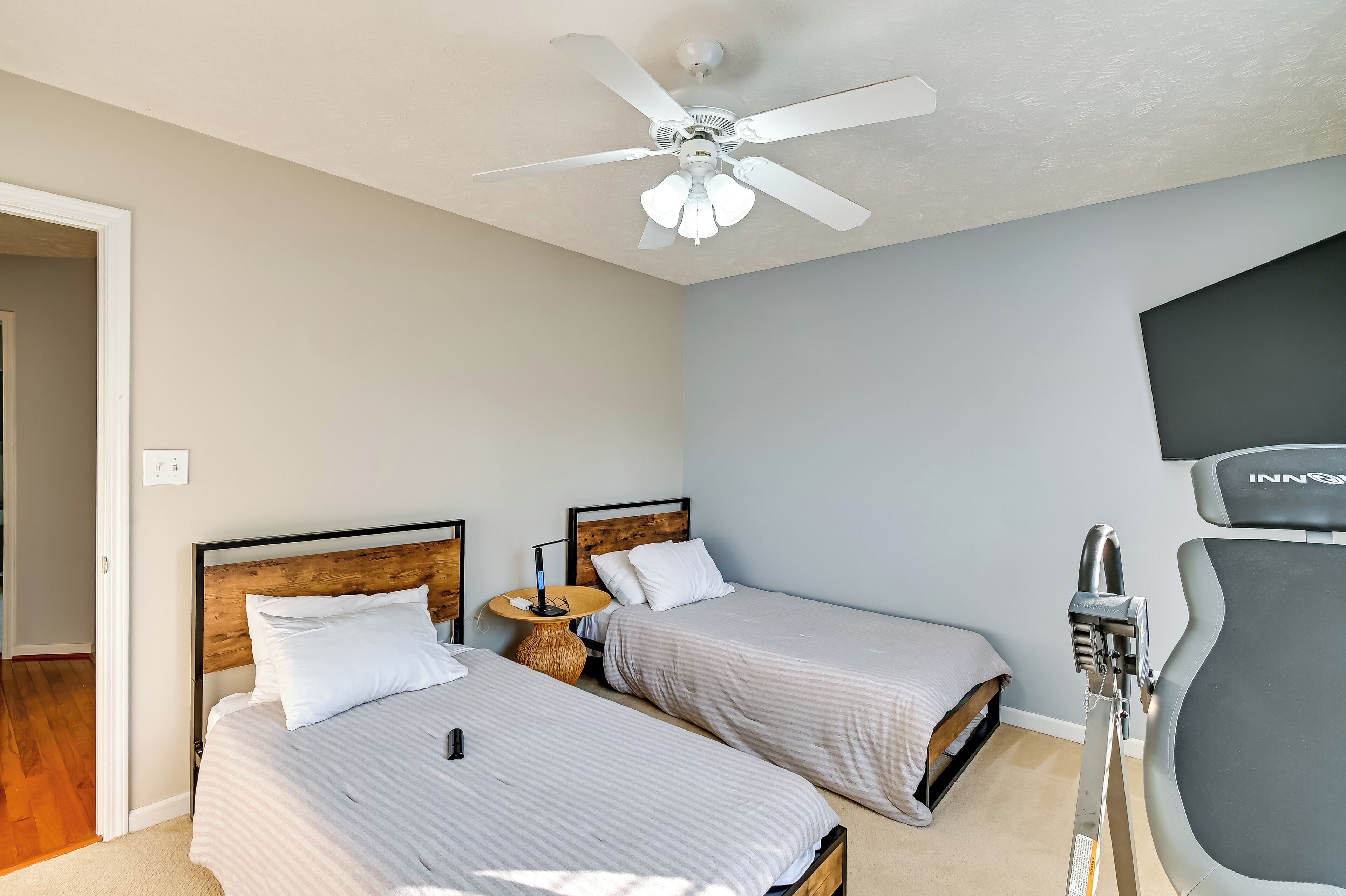 A hotel room with two beds, a ceiling fan, a small round table, and a treadmill.