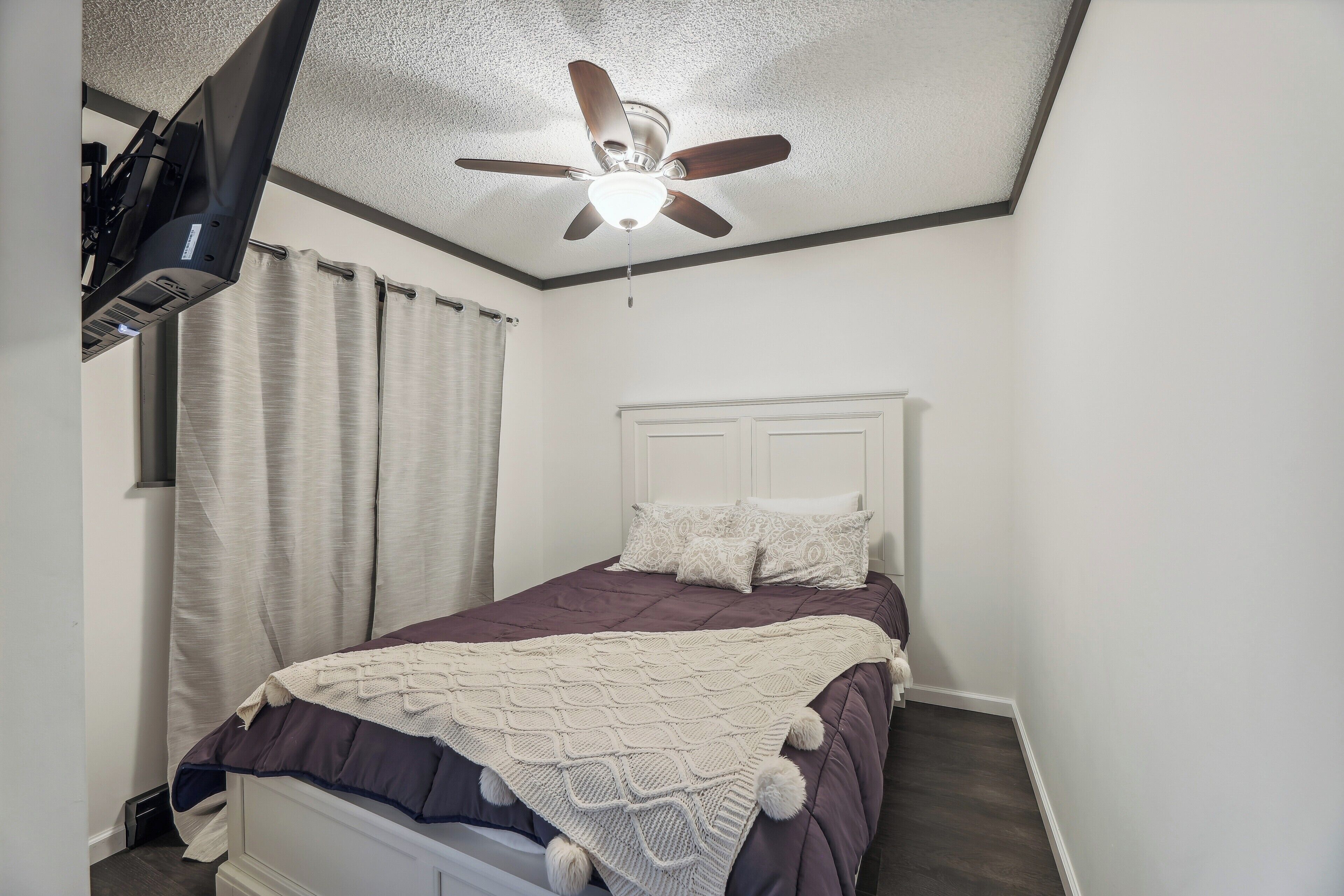 A bedroom with a bed, a ceiling fan, and a window with curtains.