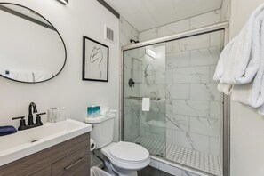 A bathroom with a white sink, a toilet, a glass shower enclosure, and a framed artwork on the wall.