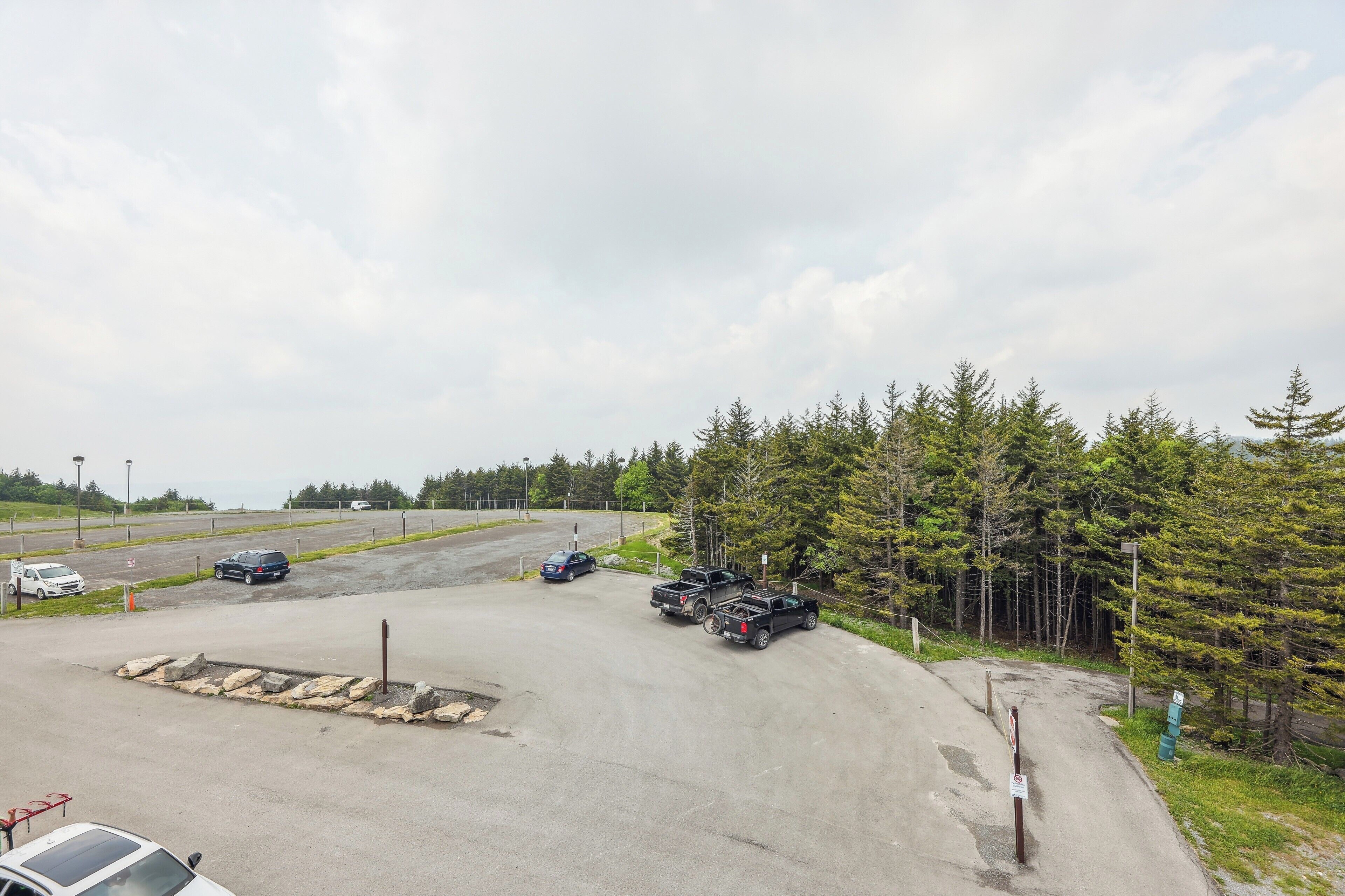 A parking lot with several vehicles, including a white van, a blue car, and two black pickup trucks.