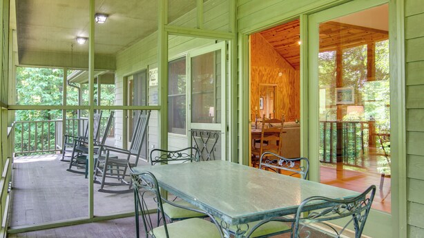A covered porch with a dining table and chairs, wooden deck, and a view of the surrounding forest. - Relaxing Saluda Home Near Waterfall Trails! (Saluda)