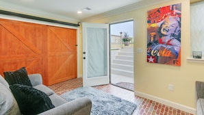 A room with a sliding door leading to a balcony, a gray sofa with a black throw pillow, and a large poster on the wall. - Rocky Vines Wine Country Retreat w/ Fire Pit (Leesburg)