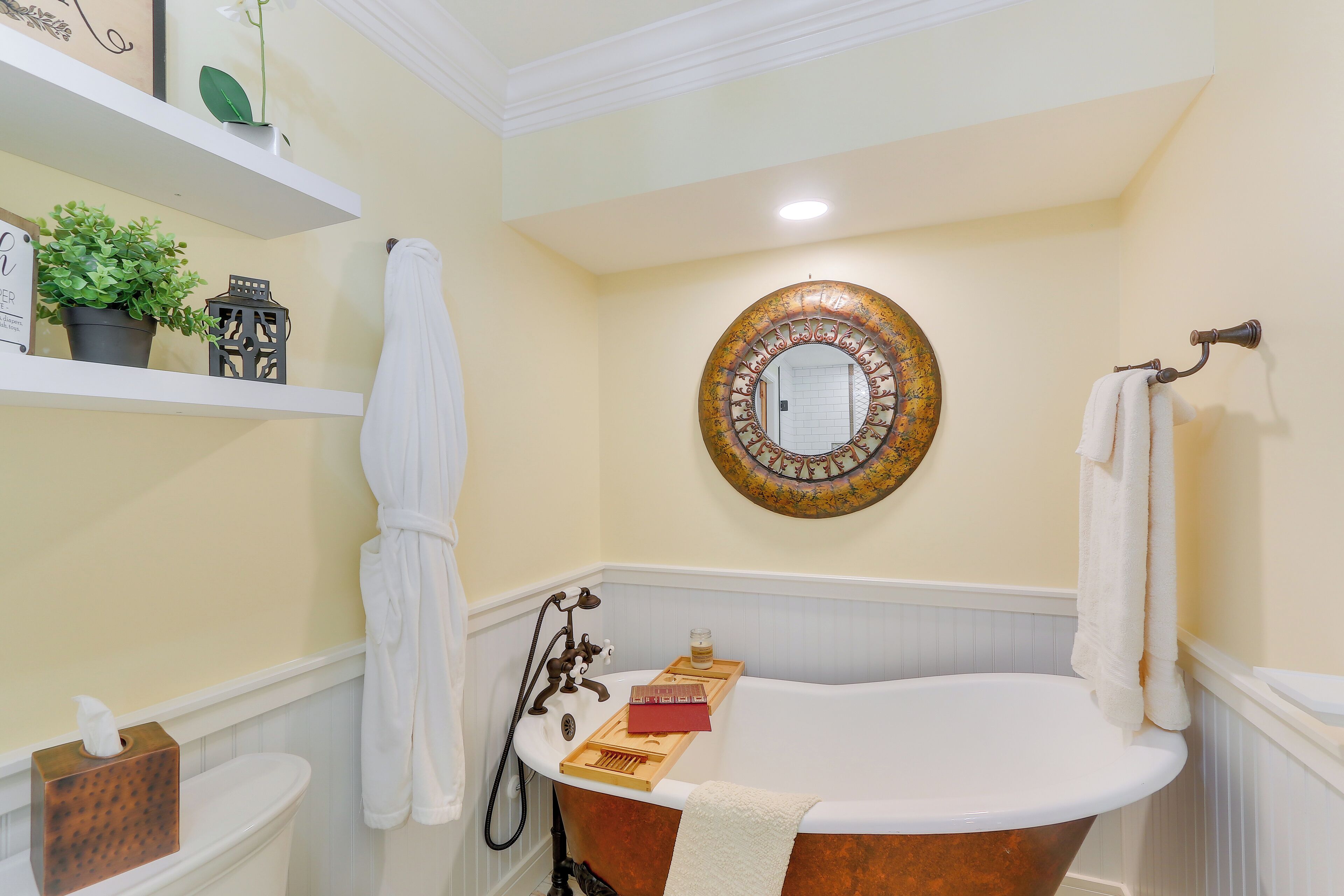 A bathroom with a freestanding bathtub, a towel rack, a mirror, and a shelf with decorative items.