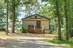 A small, single-story cabin with a front porch, situated in a wooded area with a gravel path leading to it. - Private Hot Tub & Dock: Lakefront Grove Retreat! (Grove)