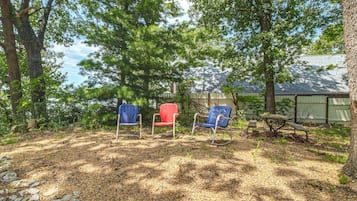An outdoor seating area with two chairs and a table, surrounded by trees and a building with a sloped roof.
