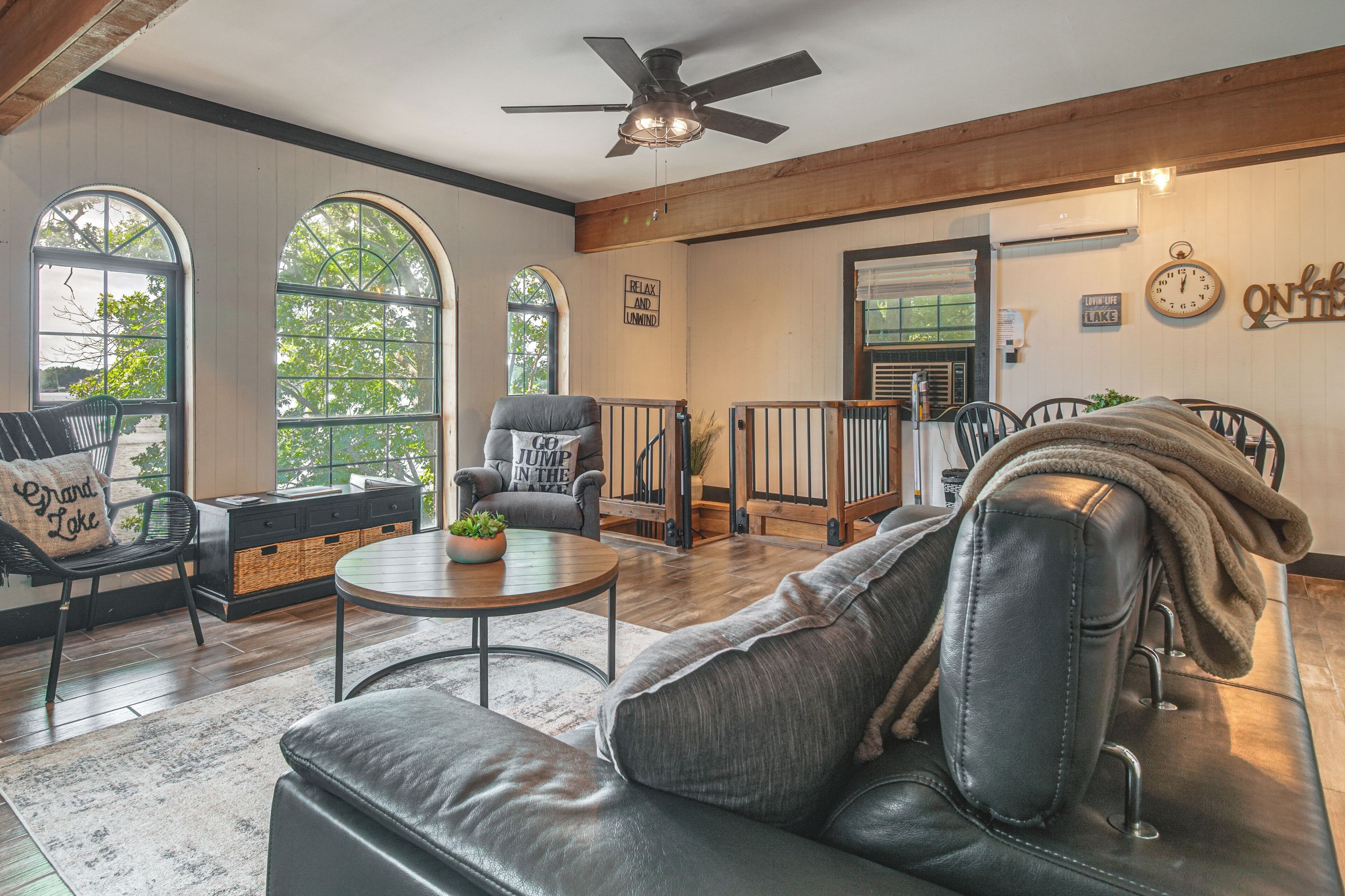 A spacious living area with a leather sofa, a round coffee table, and a view of a lake through large windows.