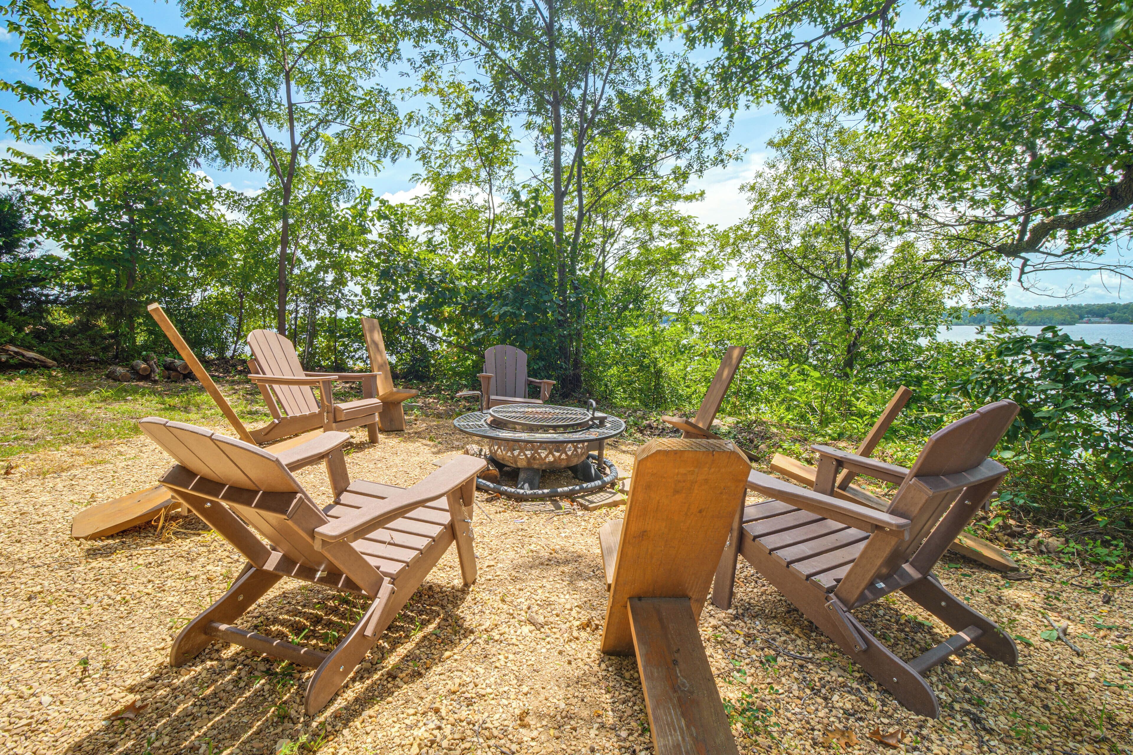 An outdoor seating area with wooden chairs and a central fire pit surrounded by trees.