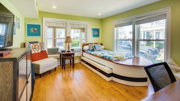 A compact bedroom with a bed, a desk, and a chair. There are windows with blinds, a lamp, and artwork on the walls. - Dewey Beach Cottage Near Ocean - Walk to Beach! (Dewey Beach)