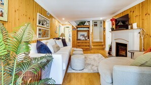 A cozy living room with wooden walls, a white sofa, a grey armchair, and a fireplace. - Dewey Beach Cottage Near Ocean - Walk to Beach! (Dewey Beach)