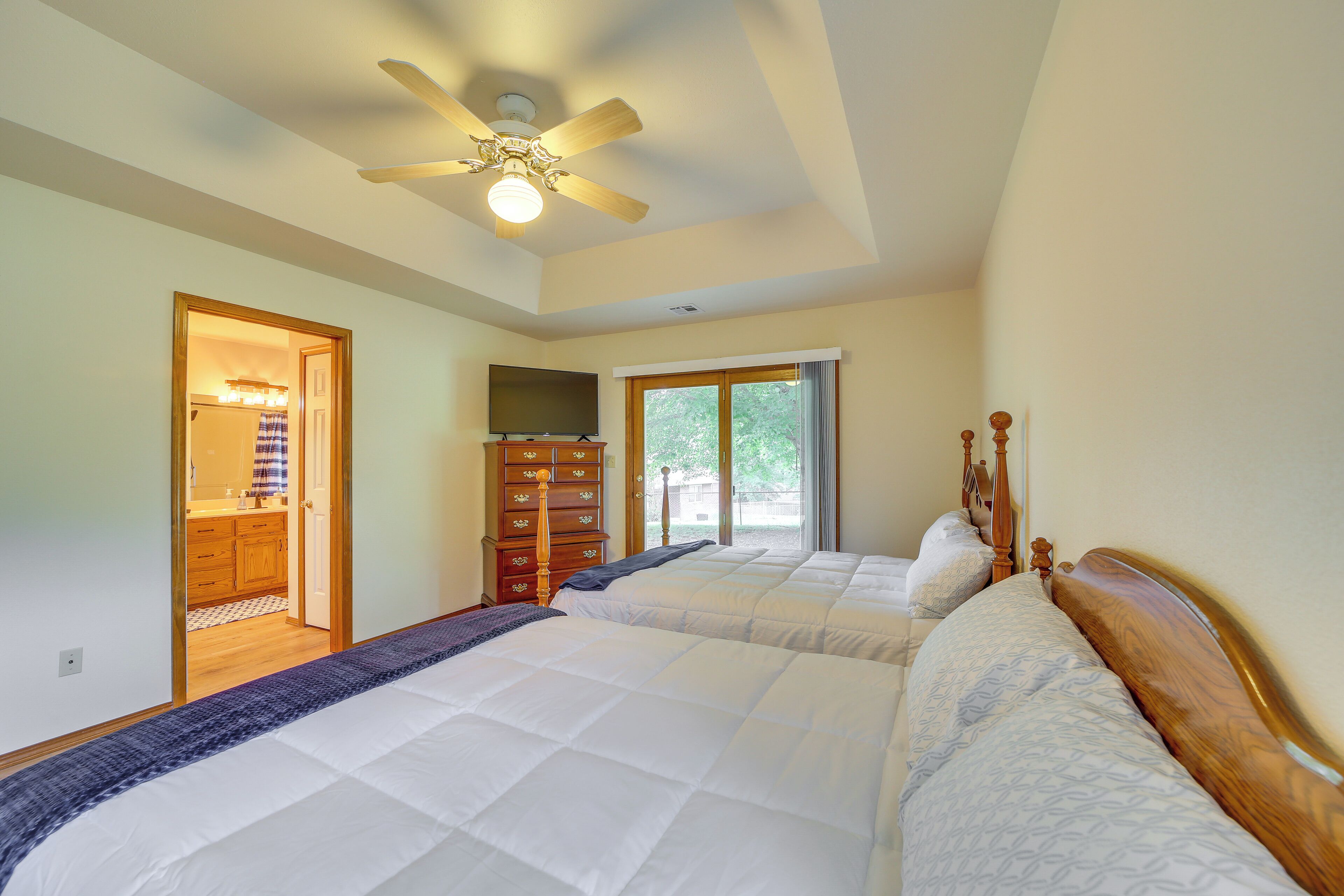 A bedroom with two beds, a ceiling fan, a dresser, and a TV.