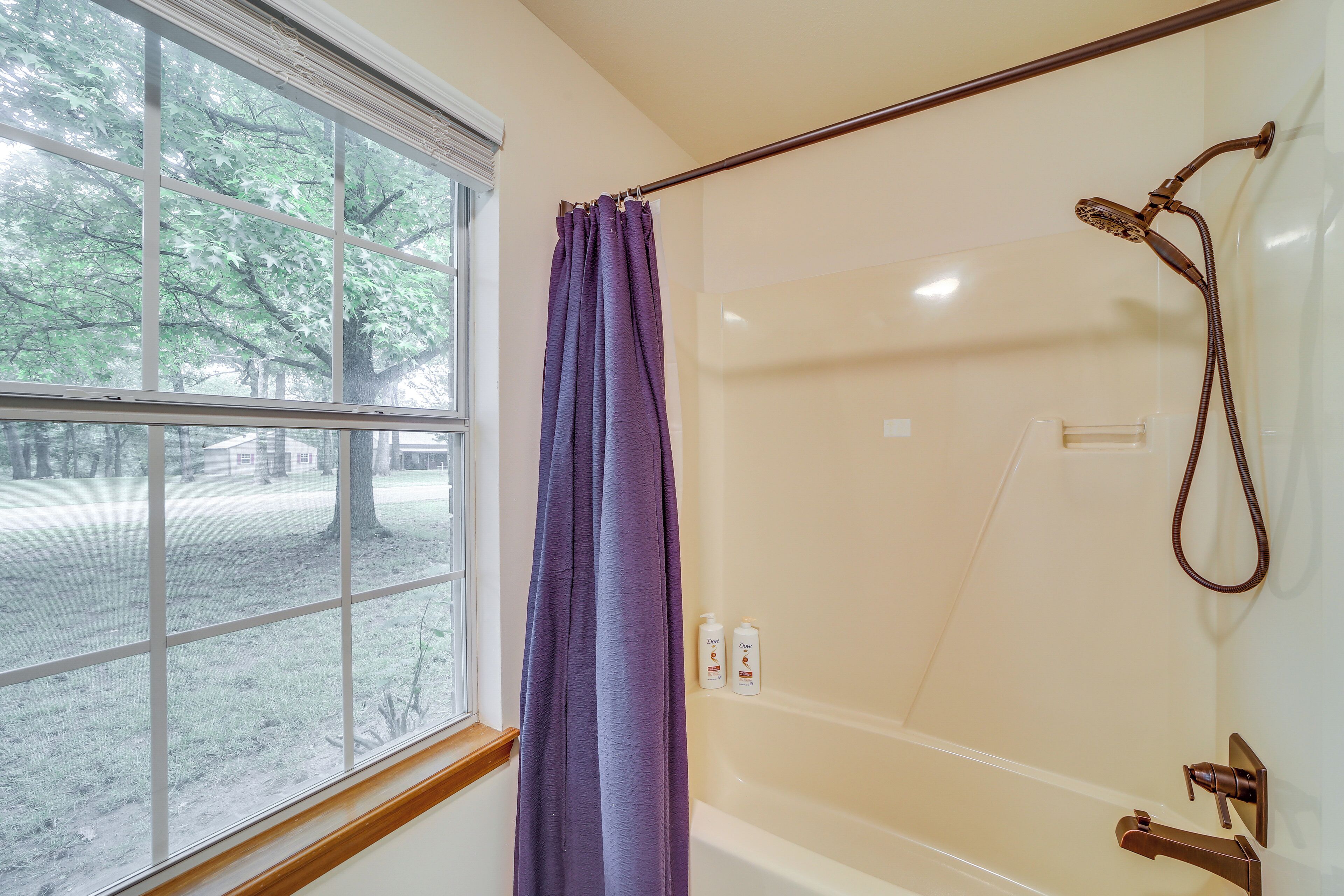 A bathroom with a bathtub, a shower, and a window with a view of trees and a building outside.