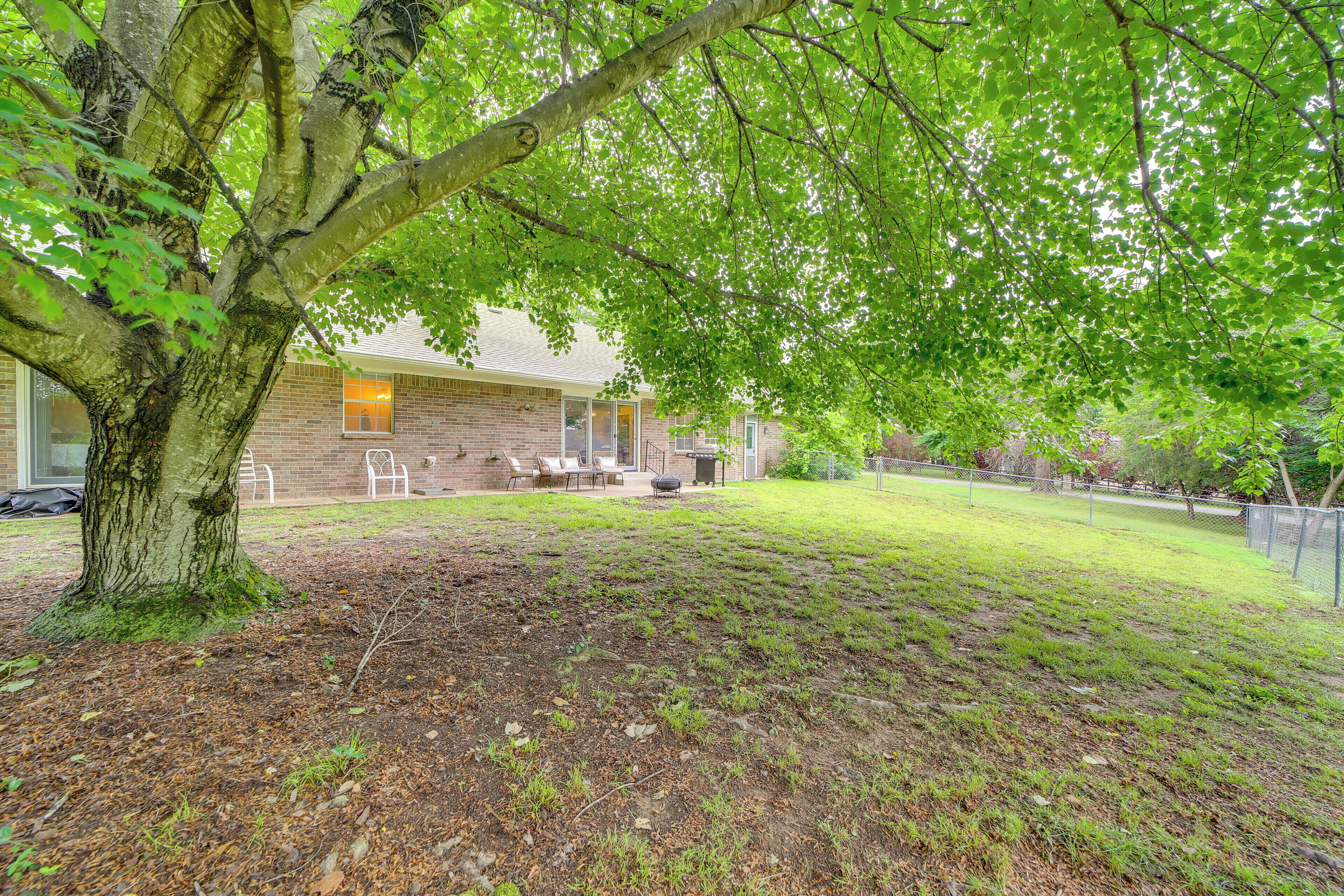 A backyard with a large tree, a brick house, and a grassy lawn.