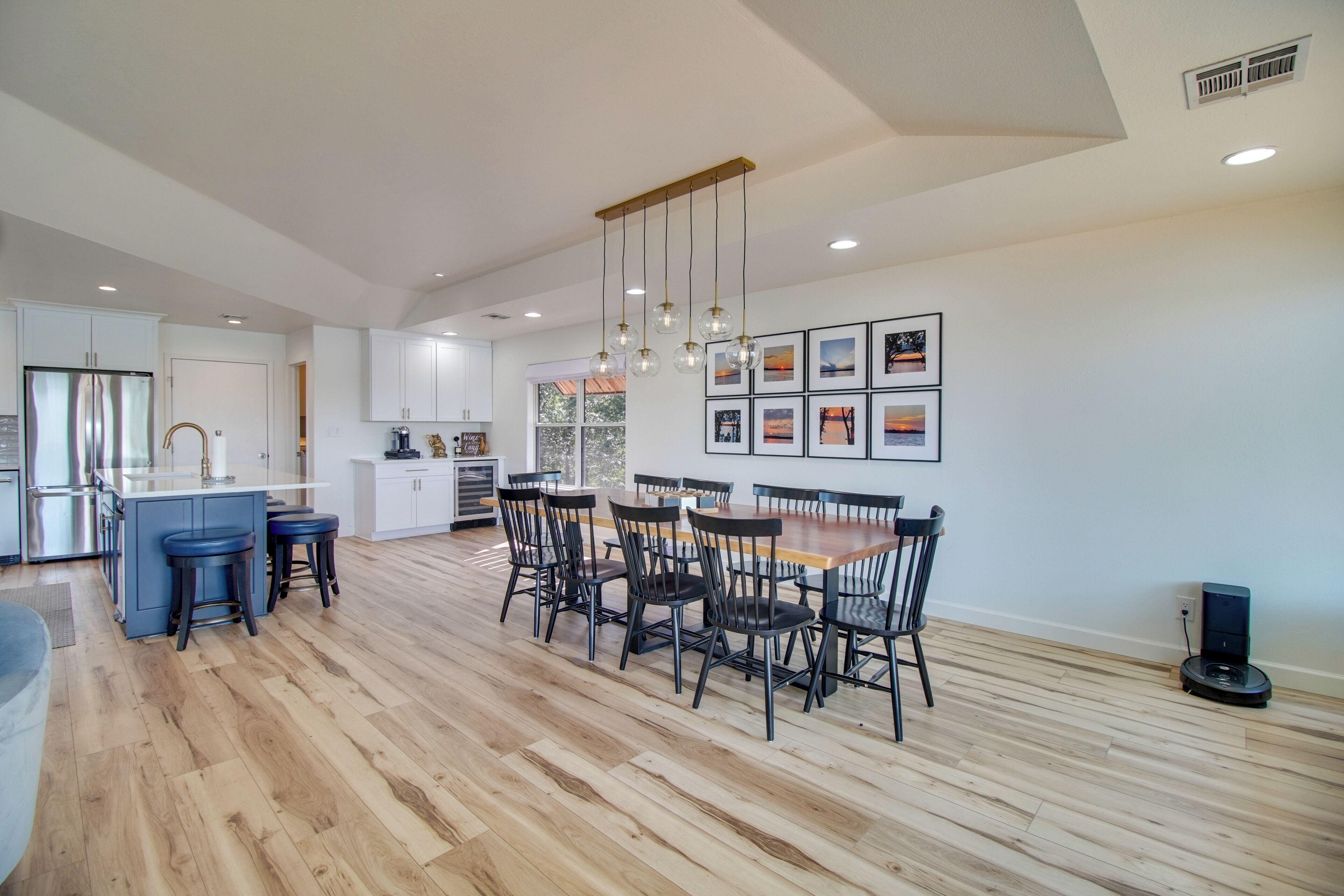 Una cocina amplia con una mesa de comedor de madera y sillas, una isla integrada con taburetes, y un ventanal que proporciona luz natural.