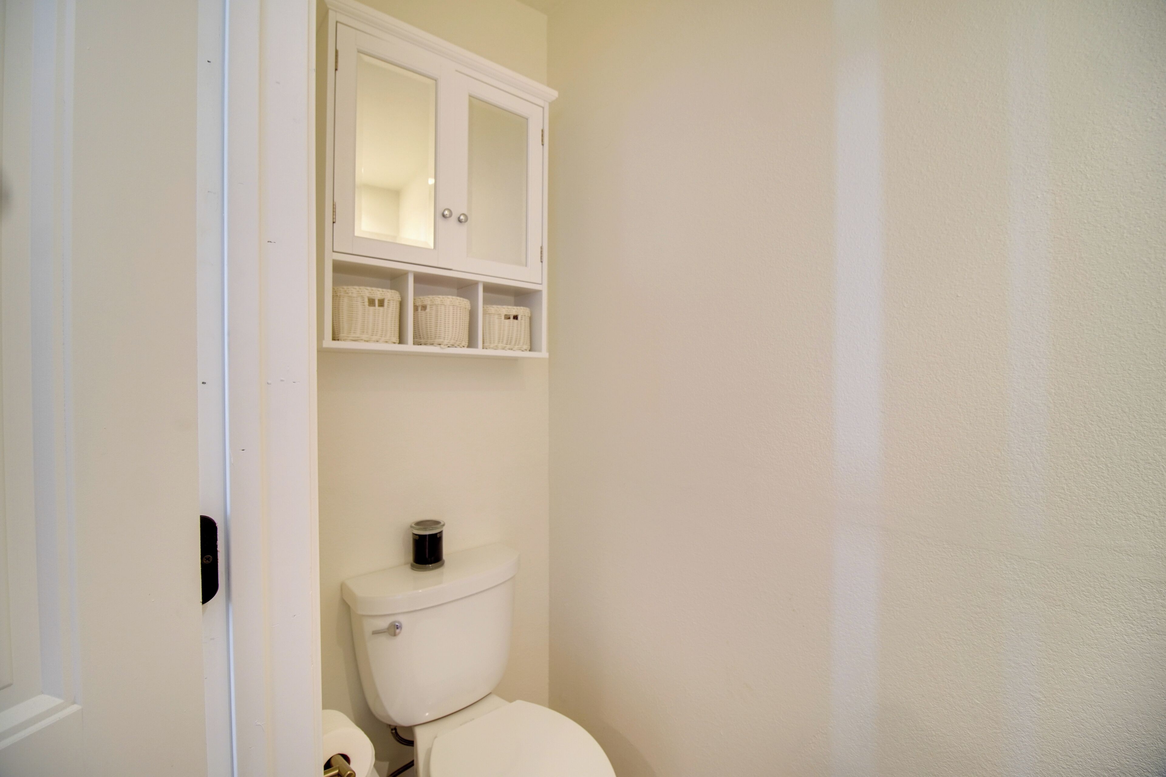 A bathroom with a toilet, a cabinet above it, and a door leading to another room.