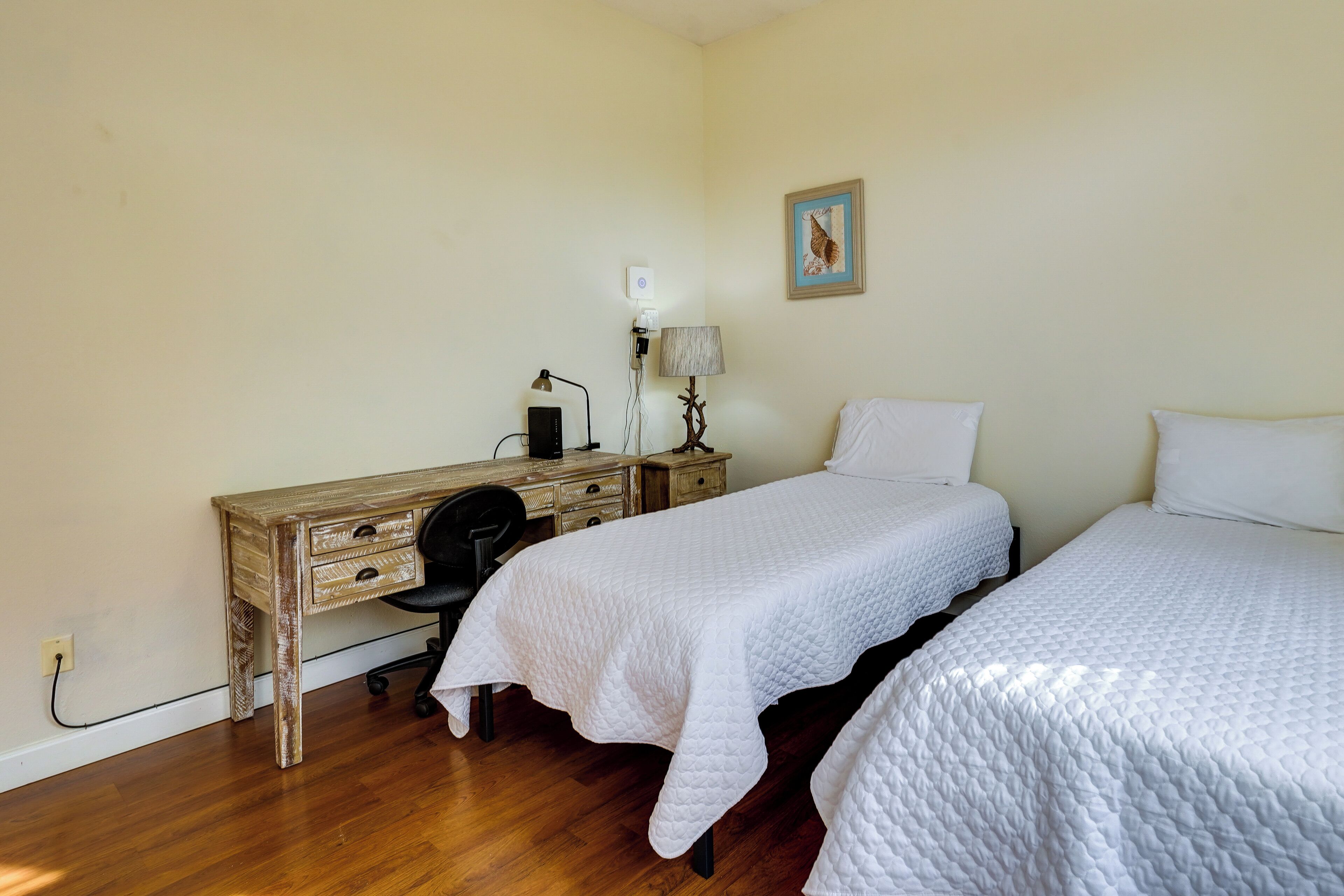 Un dormitorio con dos camas, un escritorio de madera, una silla y una lámpara.