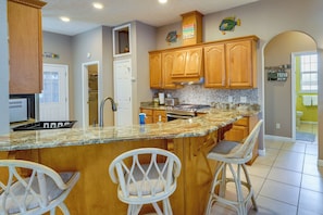 A kitchen with wooden cabinets, a granite countertop, and a large island with bar stools. - Pet-friendly Panama City Beach Home Near Beaches! (Panama City Beach)