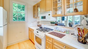 A kitchen with wooden cabinets, a stove, a microwave, and a window with a view of greenery. - 1 Mi to Indiana Dunes NP: Spacious Gary Home! (Gary)