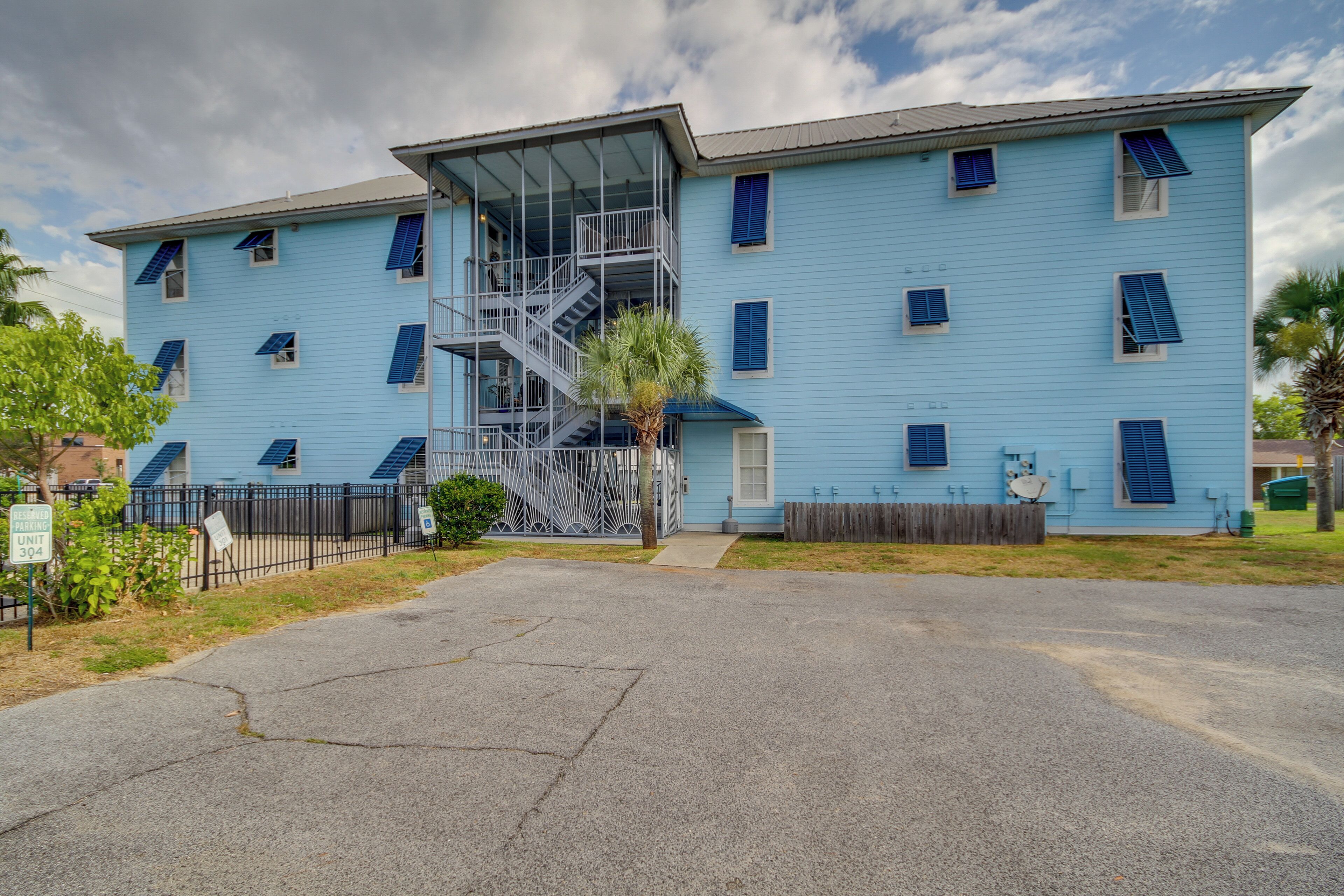 A multi-story building with a blue exterior, a central staircase, and a fenced parking area.