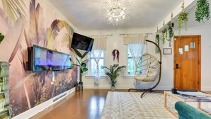 Ein geräumiges Zimmer mit einer großen Wandmalerei, einem Hängekorbstuhl, einem Fernseher und einer Holztür.