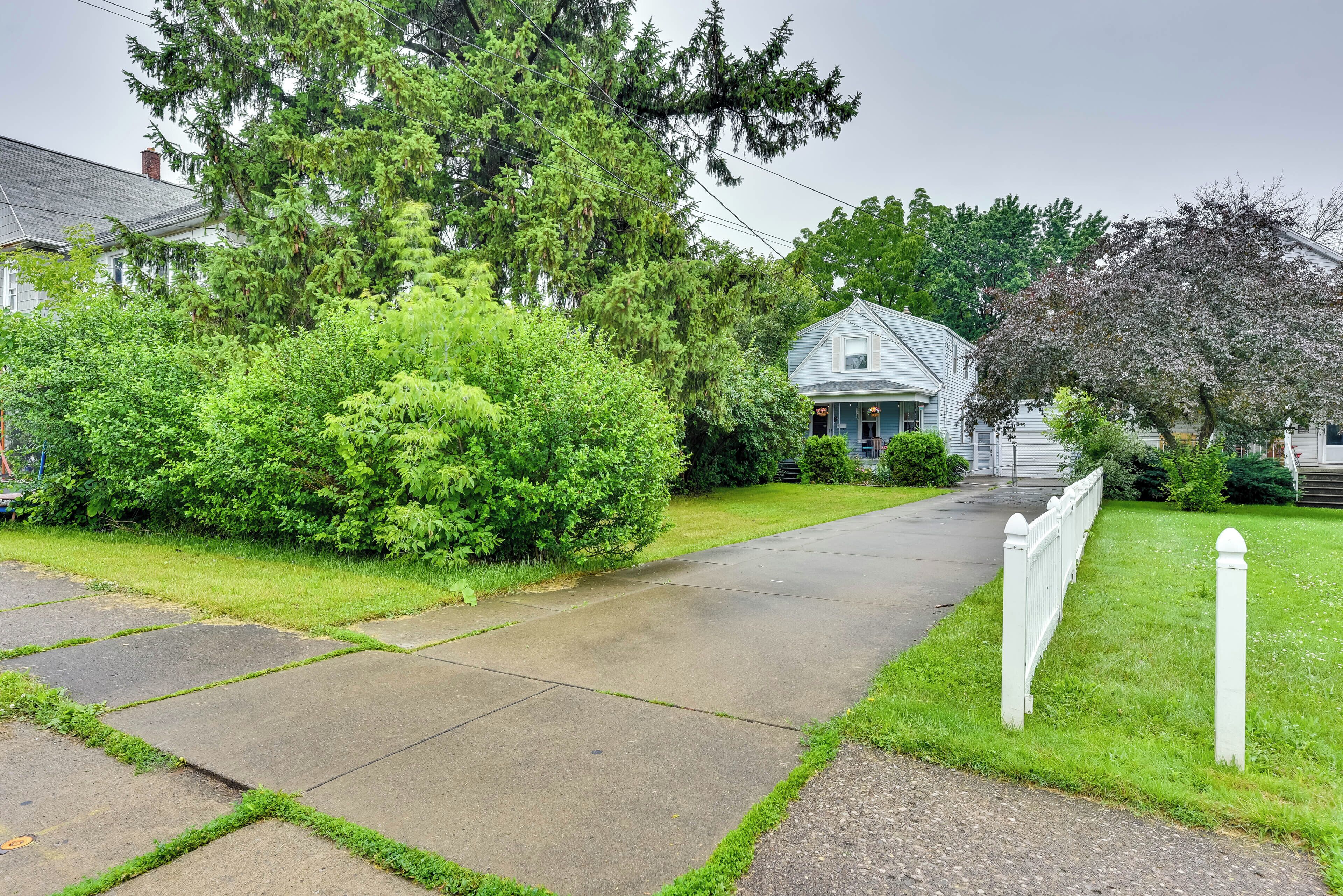 A residential driveway leading to a house with a white picket fence and lush greenery.