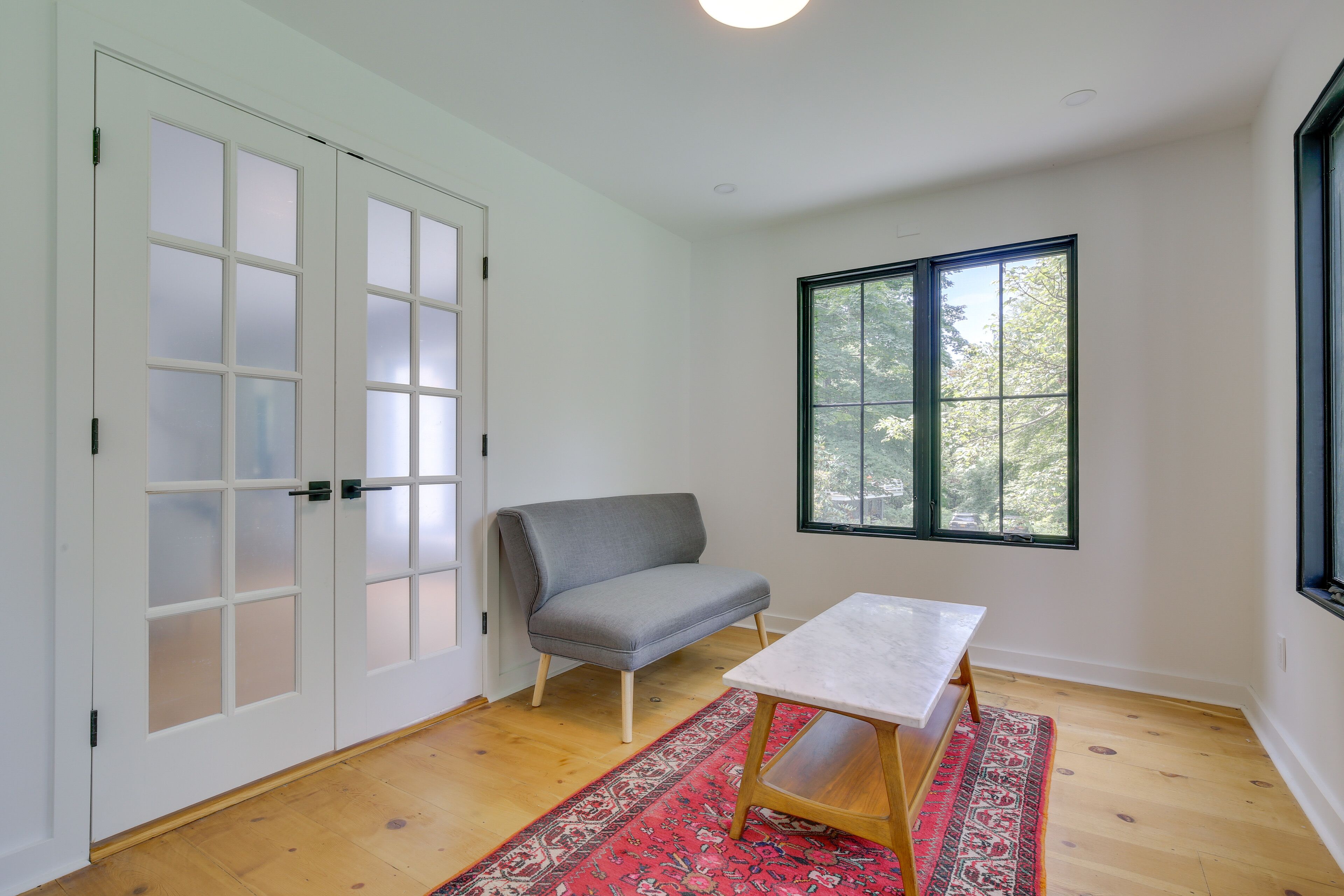 Een kamer met een grijze bank, een klein wit tafeltje en een rood vloerkleed met dessin.