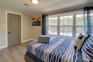 A bedroom with a large window, a bed with a blue and white striped bedspread, and a bedside table with a tissue box. - Spacious Yard, Games & Fire Pit: Grove Home Rental (Grove)