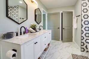 A bathroom with a white vanity, two sinks, a mirror, and a patterned shower wall. - Spacious Yard, Games & Fire Pit: Grove Home Rental (Grove)