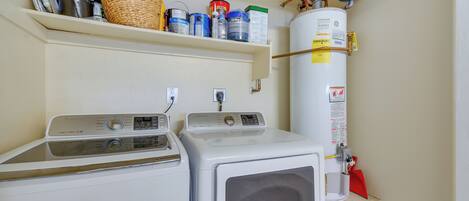 A laundry area with two washing machines, a shelf with cleaning supplies, and a water heater.