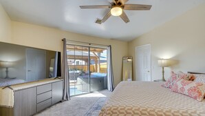 Un dormitorio con cama, cómoda, ventilador de techo, puerta corrediza de vidrio que da a un balcón y mesita de noche con lámpara.
