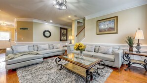 A living room with a sofa, a glass coffee table, a fluffy rug, a clock, and a framed picture on the wall.