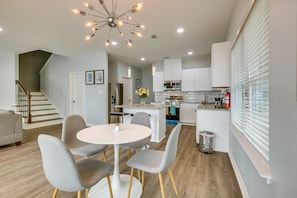 Une cuisine moderne avec des meubles blancs, un îlot central et un coin repas comprenant une table ronde et des chaises grises.