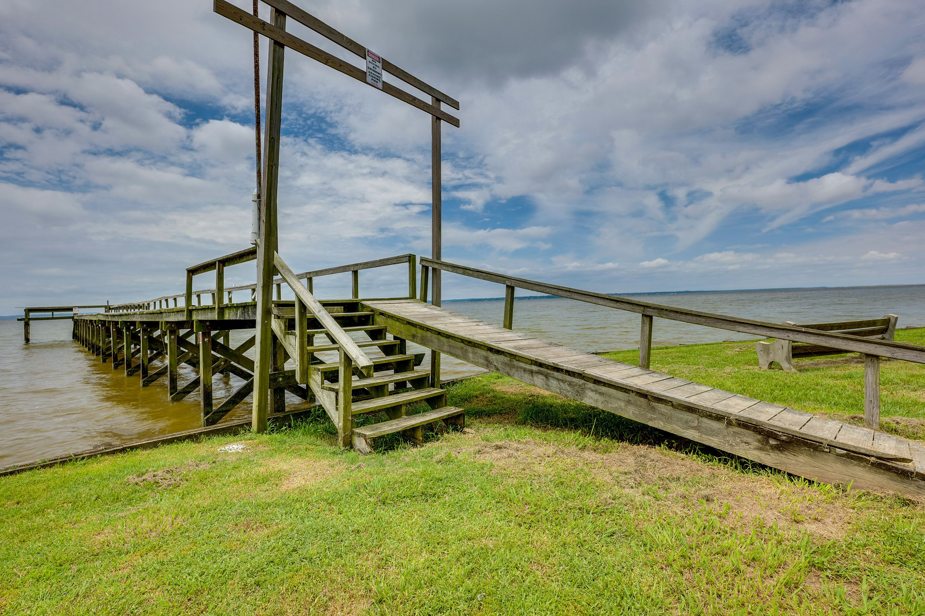 A wooden pier extending into a body of water with a grassy area in the foreground.