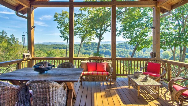 A wooden deck with wicker furniture, a table, and a view of a forested landscape. - Bryson City Condo w/ Spectacular Views & Amenities (Whittier)