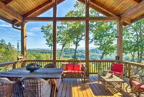 Une terrasse en bois, meublée de mobilier en osier, avec une table et une vue sur un paysage boisé.