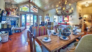 A spacious dining area with a wooden table set for four, surrounded by colorful striped sofas. A stone fireplace and a large chandelier are visible in the background. - Bryson City Condo w/ Spectacular Views & Amenities (Whittier)