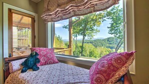 A bedroom with a large window, a bed with patterned bedding, and a teddy bear on the bed. - Bryson City Condo w/ Spectacular Views & Amenities (Whittier)