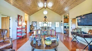 A spacious living room with a high ceiling, wooden beams, a central chandelier, a large flat-screen TV, and a cozy seating area with a sofa and armchairs. - Bryson City Condo w/ Spectacular Views & Amenities (Whittier)