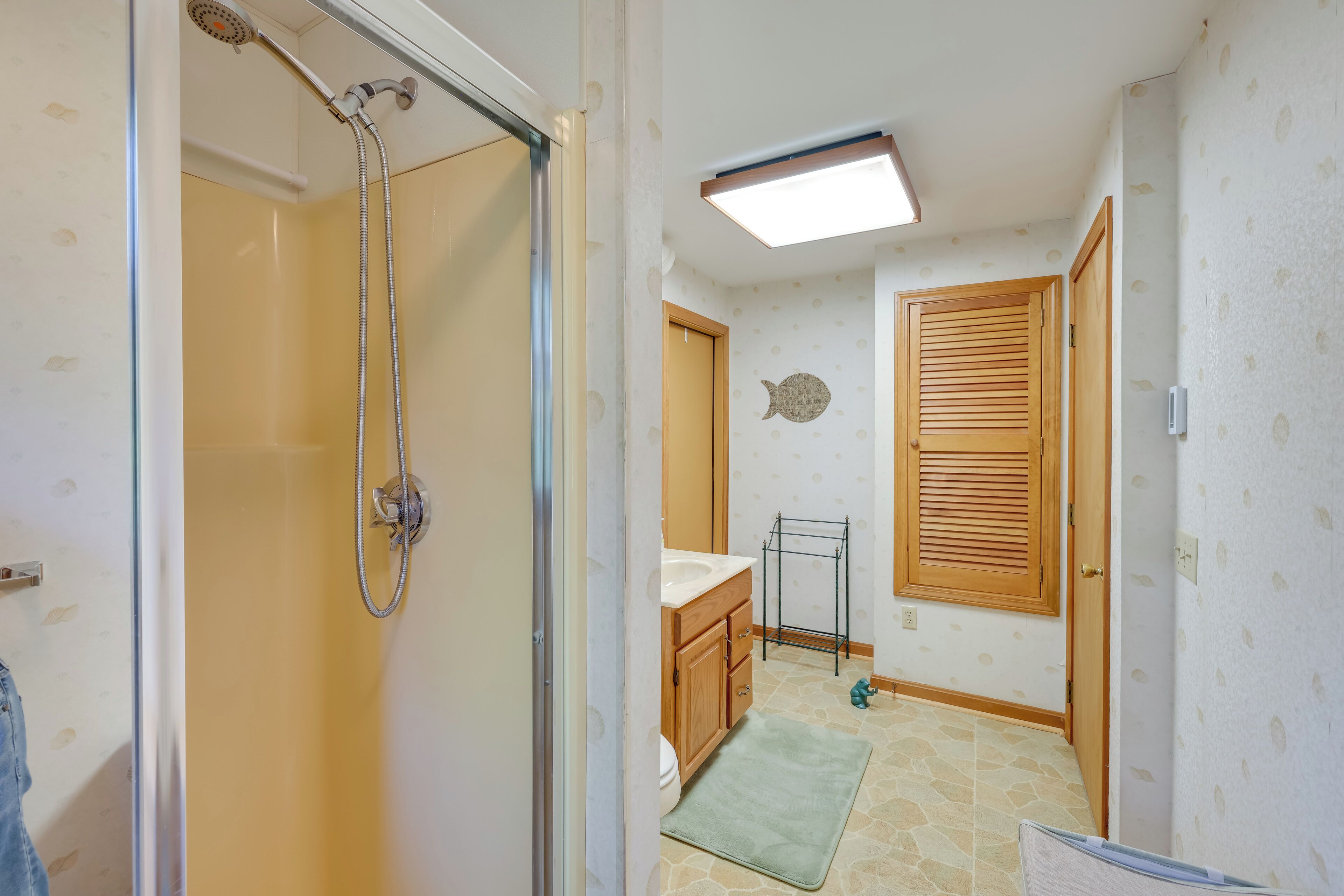 Baño con ducha, inodoro, lavamanos y armarios de madera.