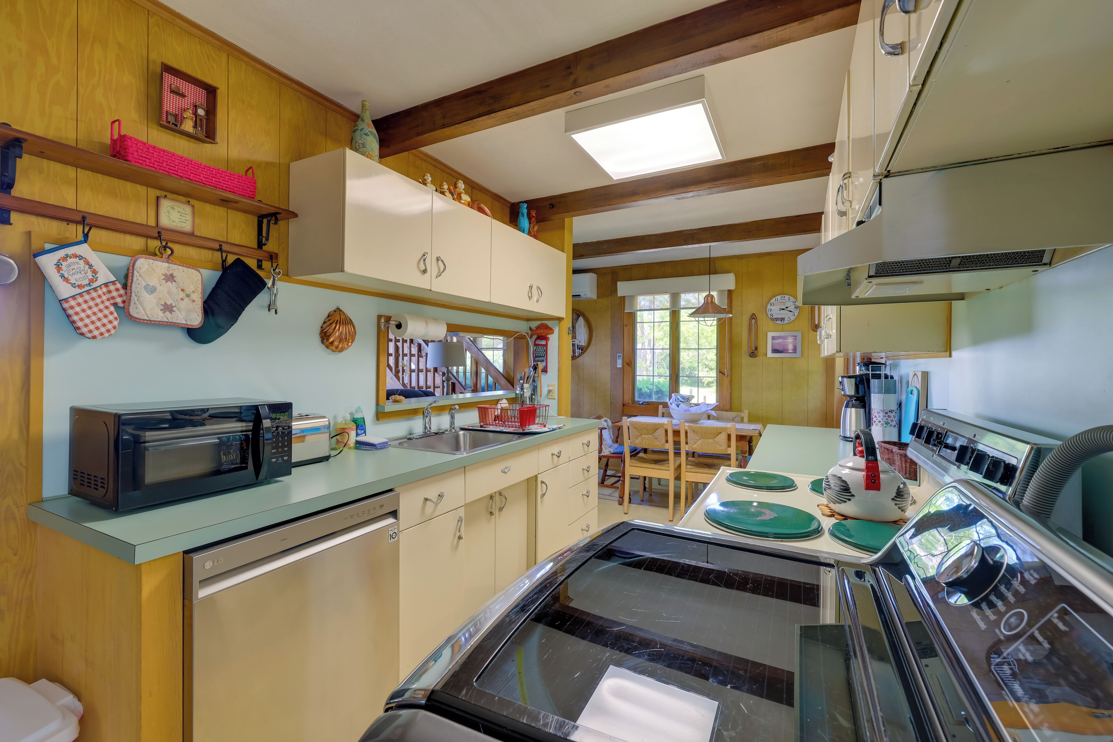 A kitchen with a microwave, stove, and wooden cabinets. There are hanging kitchen towels and a clock on the wall.